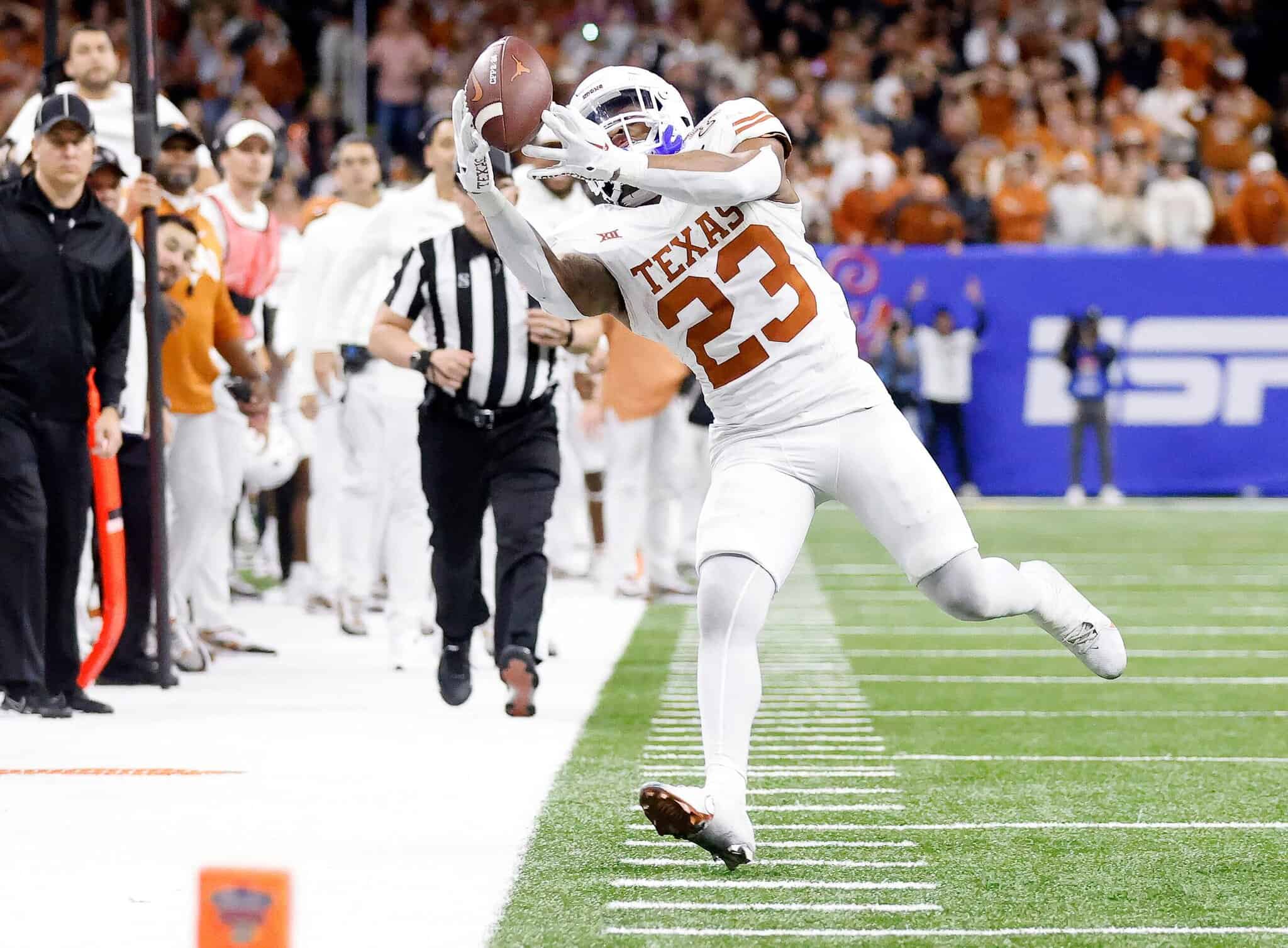 Caught in action, Texas Longhorns football player number 23 making a sideline catch during a game, surrounded by fans and referees on the field.