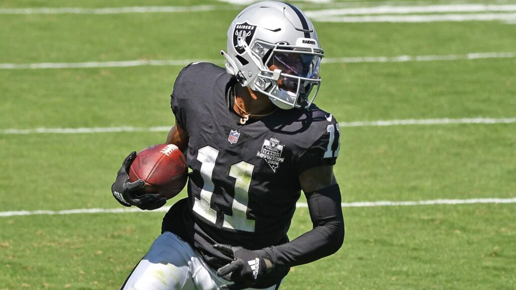 Raiders football player running with a football on the field during an NFL game.
