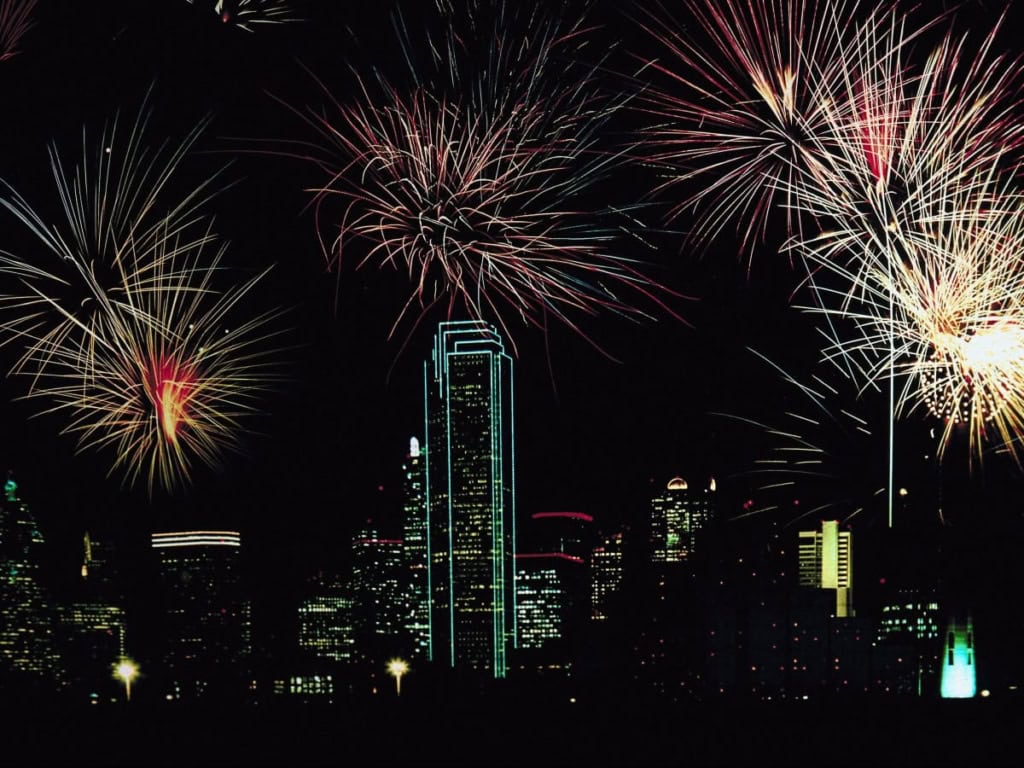 Vibrant fireworks display illuminating the Dallas skyline at night, featuring the Bank of America Plaza and other skyscrapers, celebrating with colorful explosions in the dark sky.