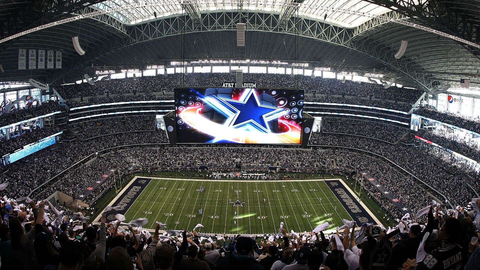 Dallas Cowboys stadium interior during a game, filled with cheering fans and a large digital screen displaying the Dallas Cowboys star logo, showcasing NFL football atmosphere.