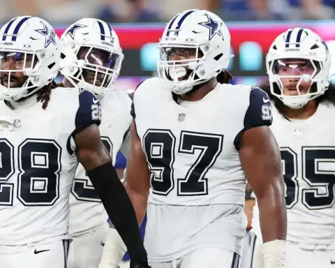Dallas Cowboys football team on the field during a game, showcasing players in white jerseys with navy blue accents, helmets with star logos, and intense focus.