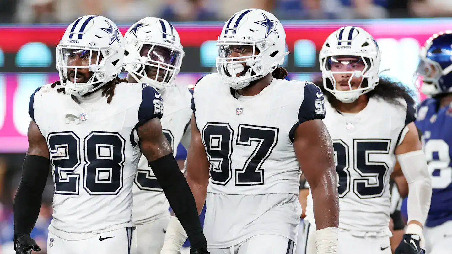 Dallas Cowboys football team on the field during a game, showcasing players in white jerseys with navy blue accents, helmets with star logos, and intense focus.