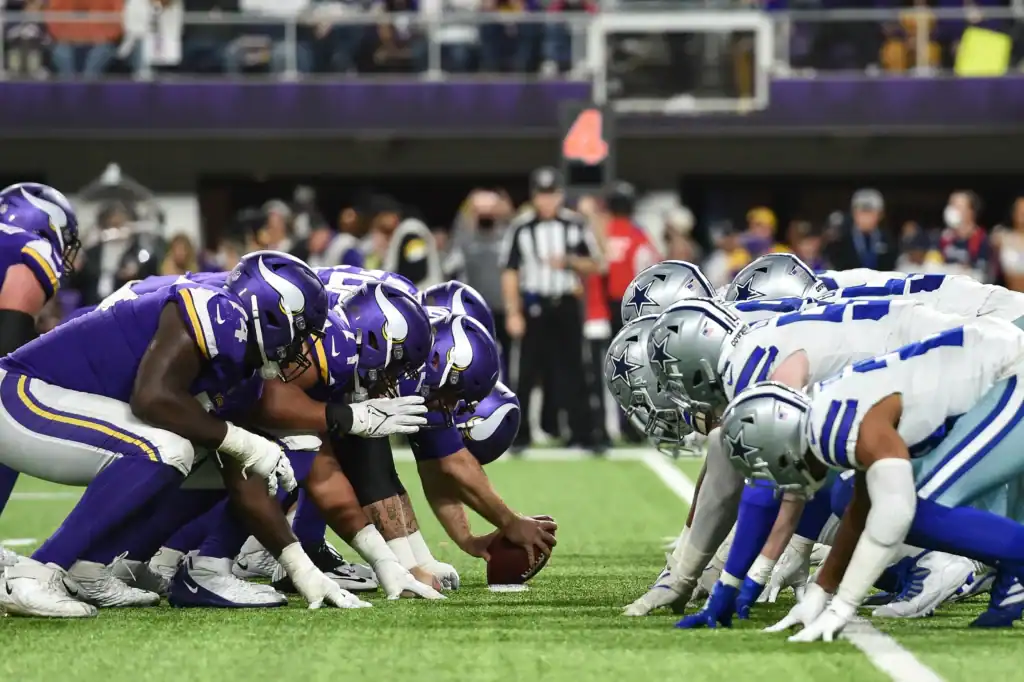 Rushing players from the Minnesota Vikings and Dallas Cowboys line up at the line of scrimmage during an NFL game, showcasing intense team rivalry and game strategy on the football field.