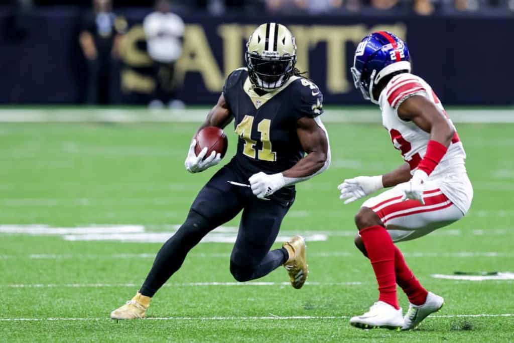 Running back in action during an NFL game, wearing a black jersey with the number 41 for the New Orleans Saints, evades a defender from the New York Giants in white and red.