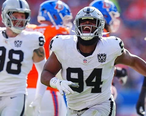 A football player from the Las Vegas Raiders celebrating during a game, surrounded by teammates, in a competitive NFL environment. The player wears a white jersey with the number 94 and a Raider helmet, highlighting team spirit and athletic performance.