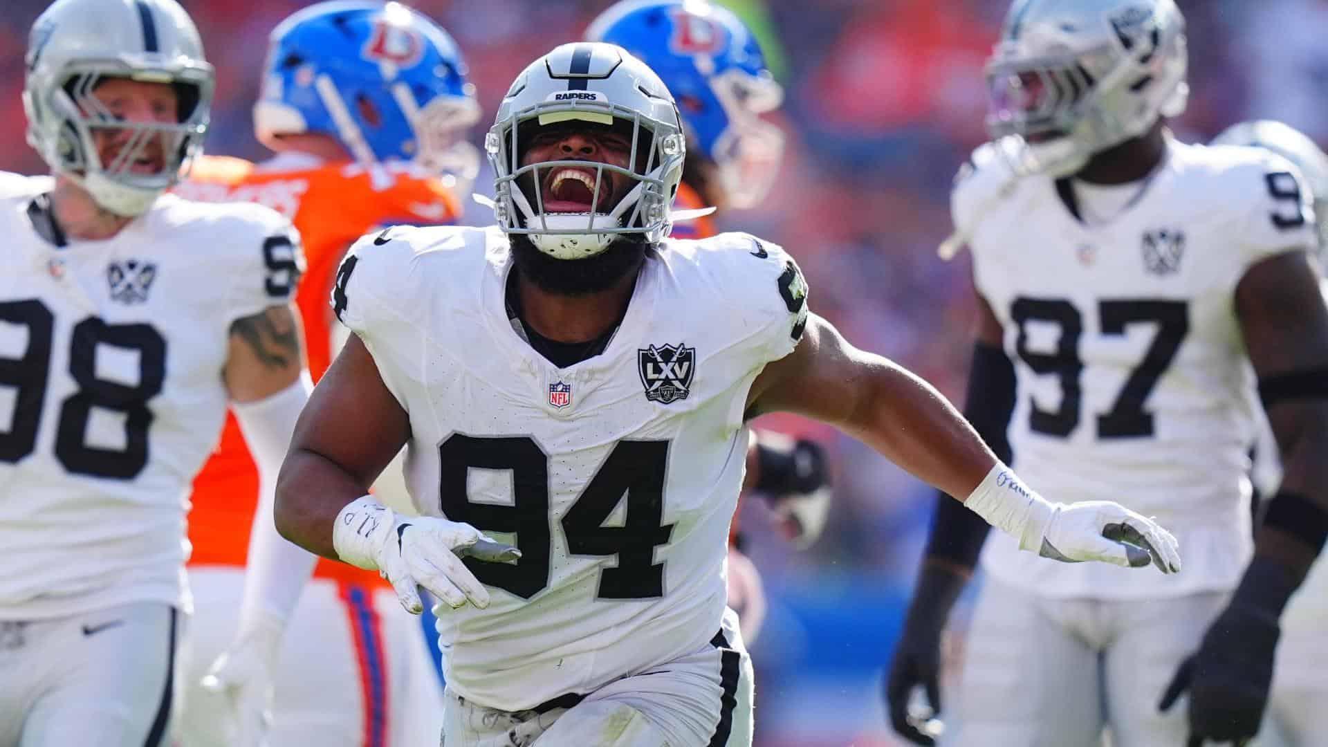 A football player from the Las Vegas Raiders celebrating during a game, surrounded by teammates, in a competitive NFL environment. The player wears a white jersey with the number 94 and a Raider helmet, highlighting team spirit and athletic performance.