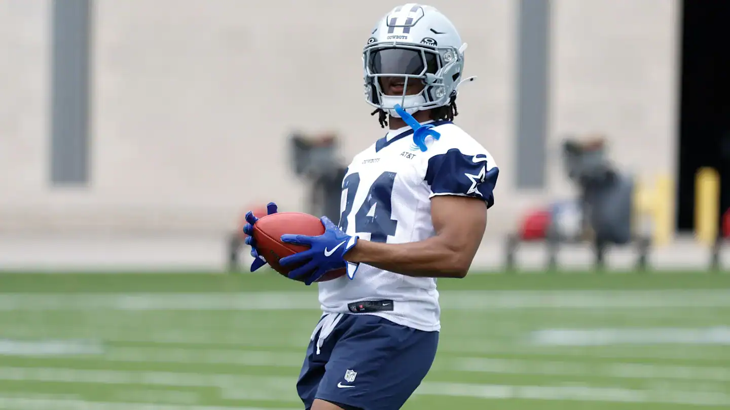 High school football player in Dallas Cowboys uniform holding football during practice.