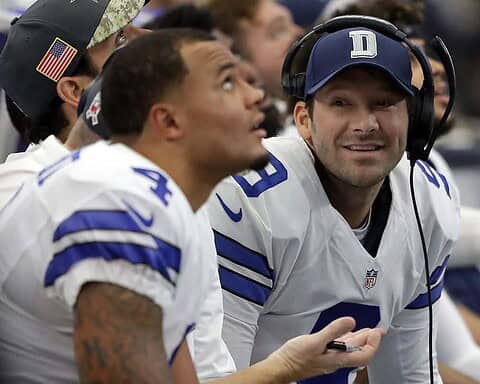 Dallas Cowboys sideline during an NFL game, featuring players and coaching staff in team jerseys, with focus on the coaching staff's interactions, showcasing team strategy and communication.