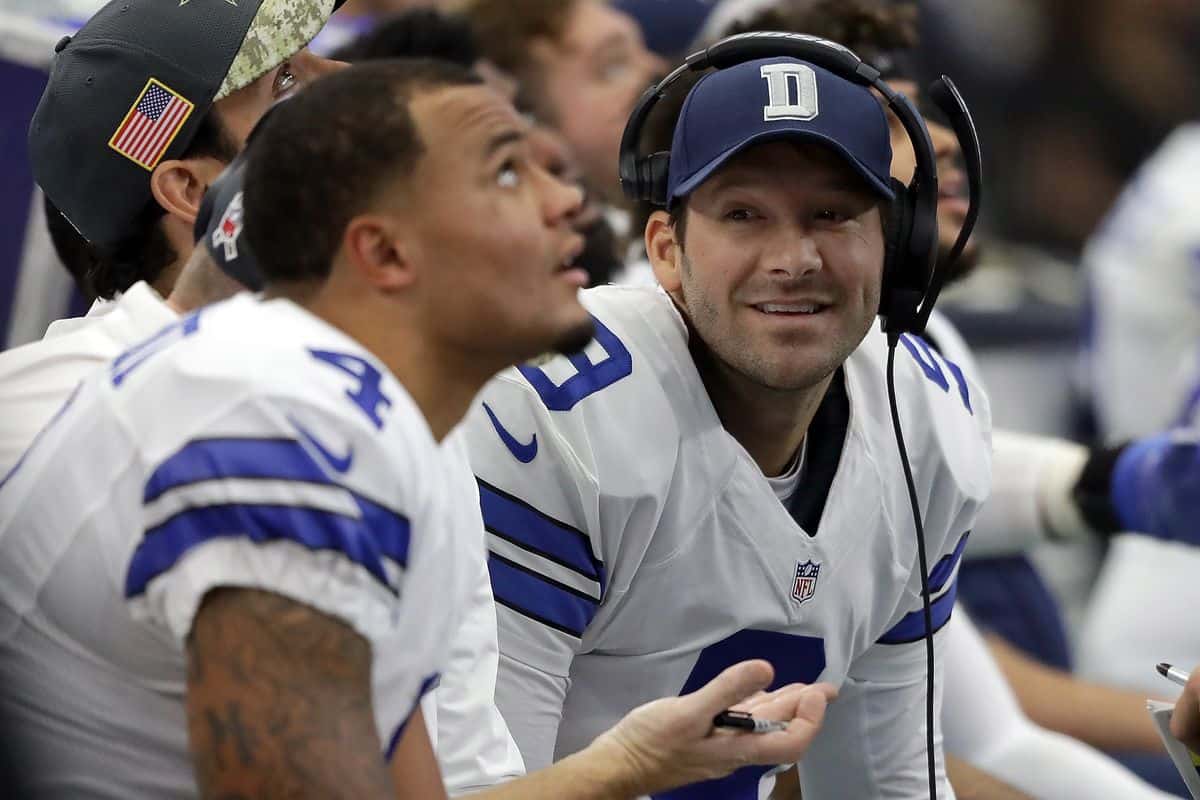 Dallas Cowboys sideline during an NFL game, featuring players and coaching staff in team jerseys, with focus on the coaching staff's interactions, showcasing team strategy and communication.