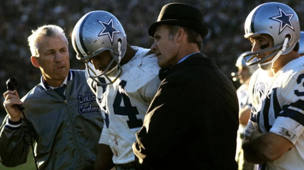 Upset Dallas Cowboys player receiving medical attention during football game with coaches and medical staff on sidelines.