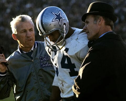 Upset Dallas Cowboys player receiving medical attention during football game with coaches and medical staff on sidelines.