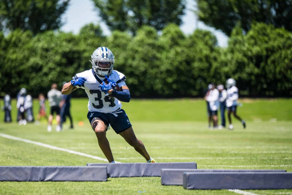 Young football player practicing at training camp with Dallas Cowboys gear on a sunny day.