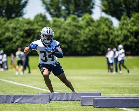Young football player practicing at training camp with Dallas Cowboys gear on a sunny day.