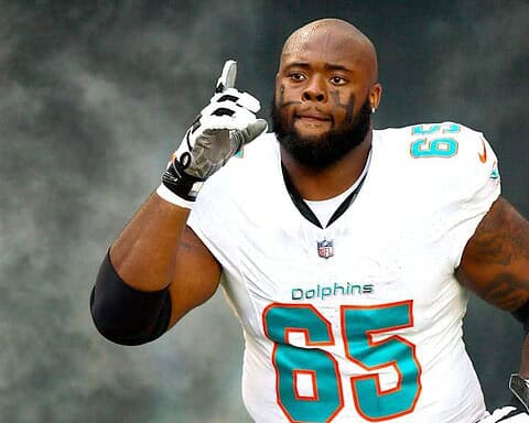 - NFL player on field wearing Miami Dolphins uniform, making a gesture near his ear, during a game.