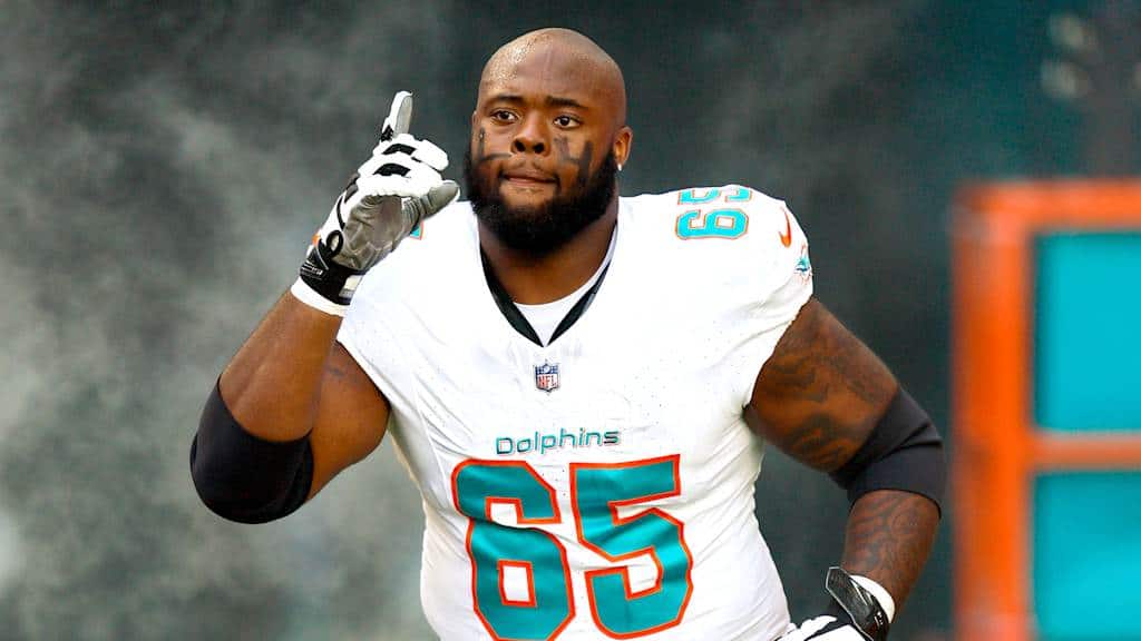 - NFL player on field wearing Miami Dolphins uniform, making a gesture near his ear, during a game.