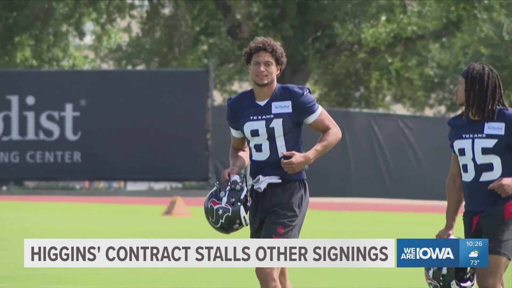 Houston Texans football player during practice at the training facility, wearing jersey number 81, holding helmet, with another player nearby and football field background.