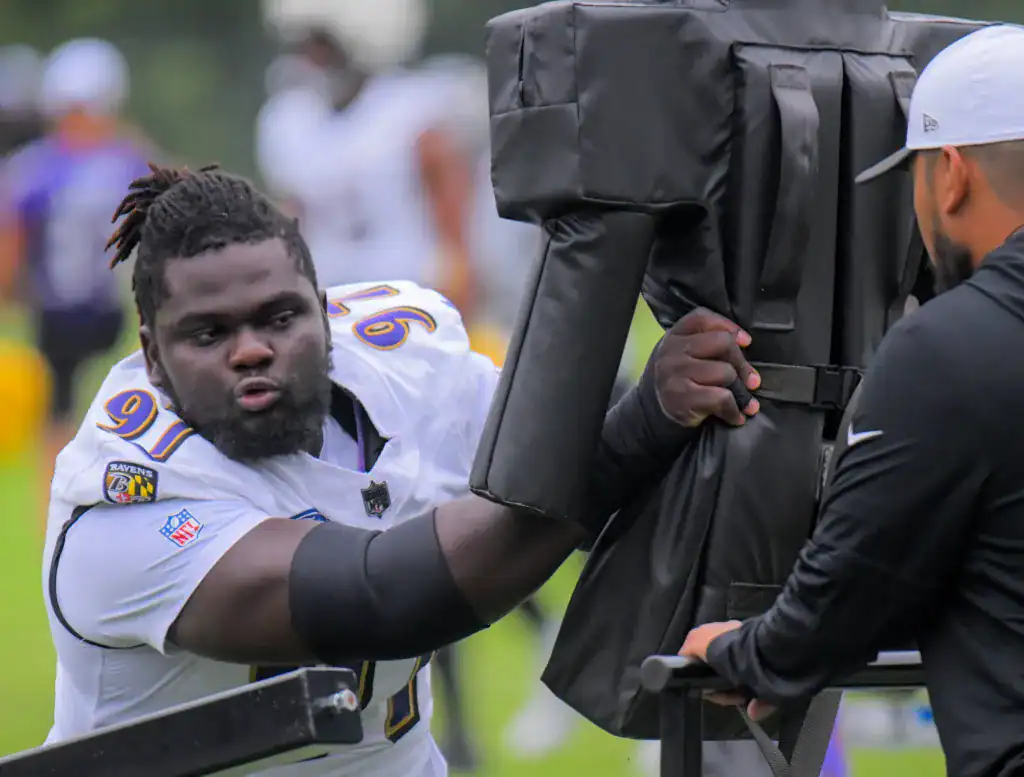 - Young football player practicing training drills with tackling dummy at practice field.
