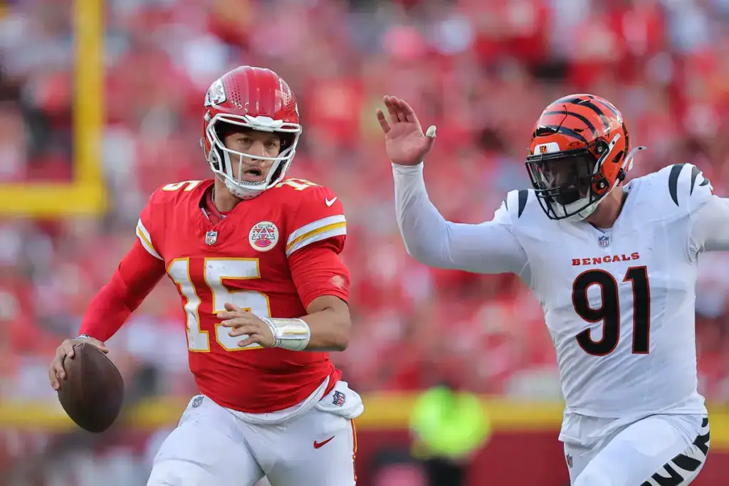 Quarterback Patrick Mahomes of the Kansas City Chiefs in action during an NFL game, wearing a red jersey and helmet, holding the football, with Cincinnati Bengals defender in pursuit.