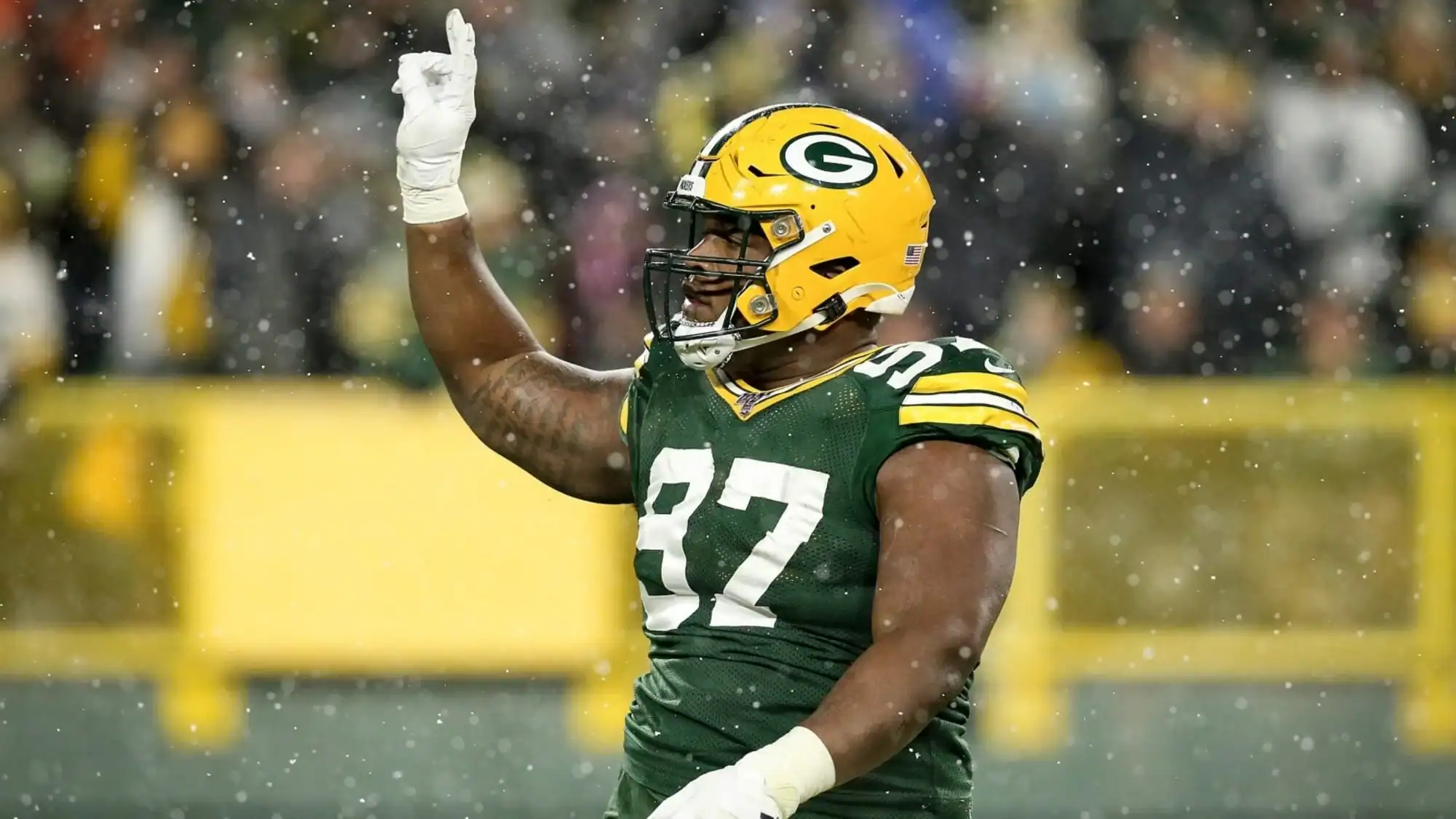 Green Bay Packers football player wearing yellow helmet and dark green jersey with the number 32, celebrating on the field during a game in the rain.