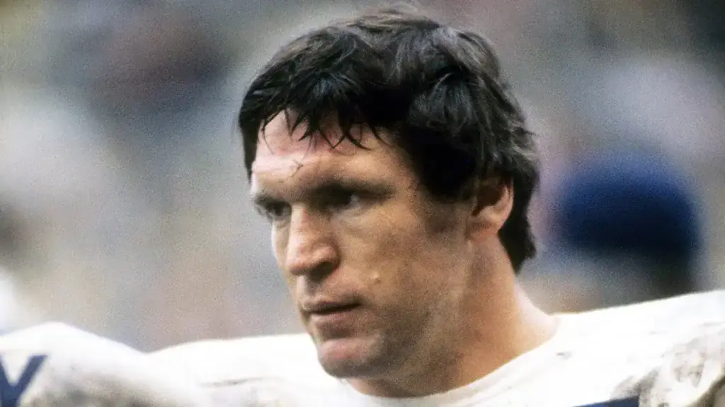 A close-up of a football player with dark hair and intense focus, wearing a white jersey, during a game at Inside The Star, Dallas Cowboys stadium, highlighting sports analysis and NFL athlete coverage.