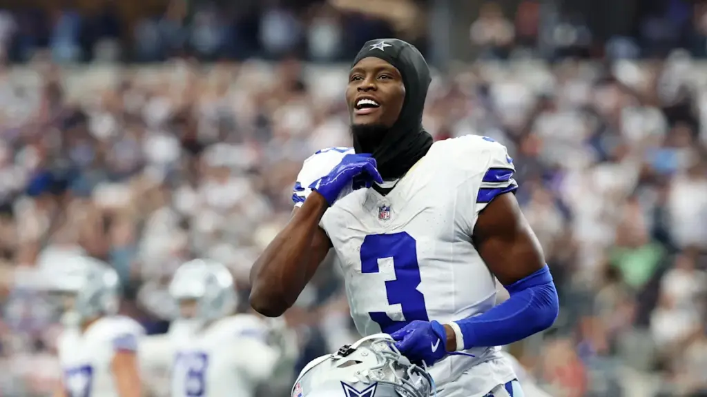 Athletic Dallas Cowboys player celebrating on the field during an NFL game, wearing team uniform and helmet, with fans in the background.