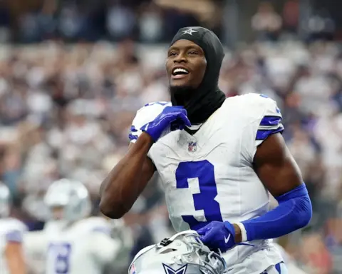 Athletic Dallas Cowboys player celebrating on the field during an NFL game, wearing team uniform and helmet, with fans in the background.