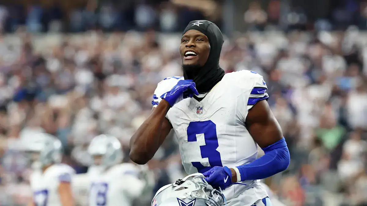 Athletic Dallas Cowboys player celebrating on the field during an NFL game, wearing team uniform and helmet, with fans in the background.