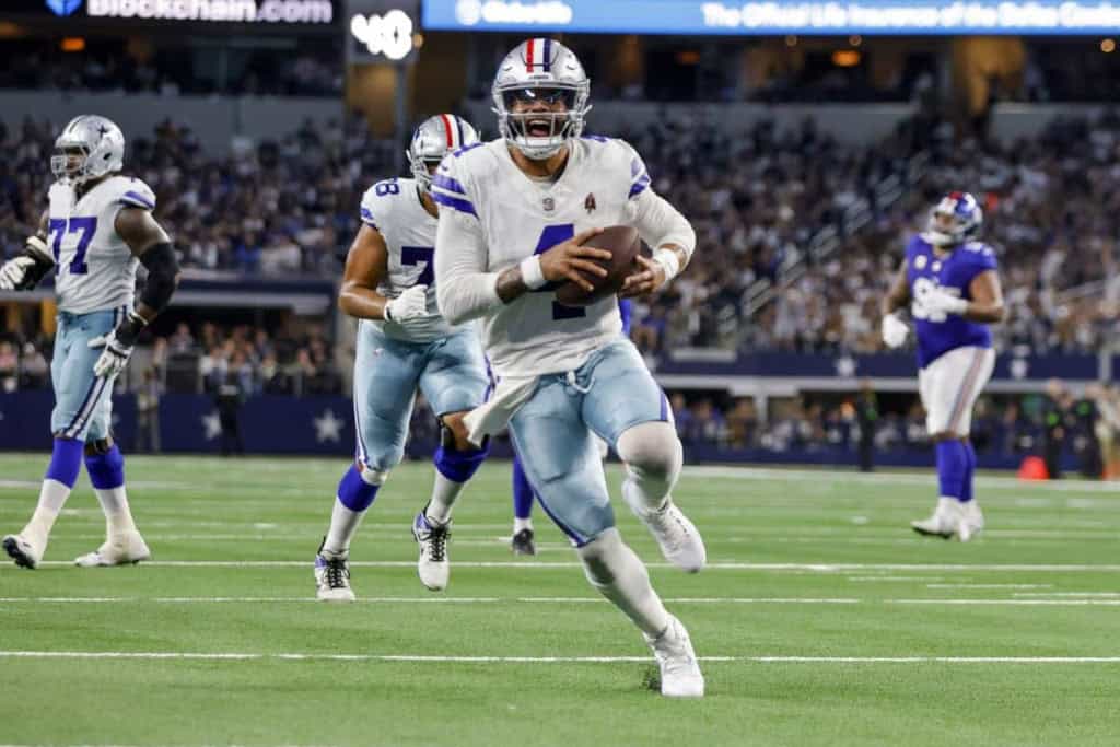 Dallas Cowboys player running with football during game, NFL football action, team in white and blue uniforms, stadium atmosphere, inside the star.