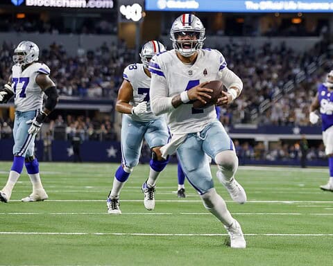 Dallas Cowboys player running with football during game, NFL football action, team in white and blue uniforms, stadium atmosphere, inside the star.
