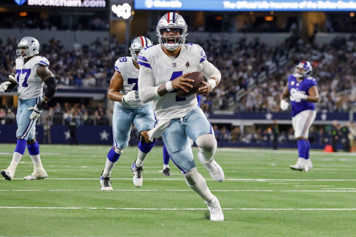 Dallas Cowboys player running with football during game, NFL football action, team in white and blue uniforms, stadium atmosphere, inside the star.
