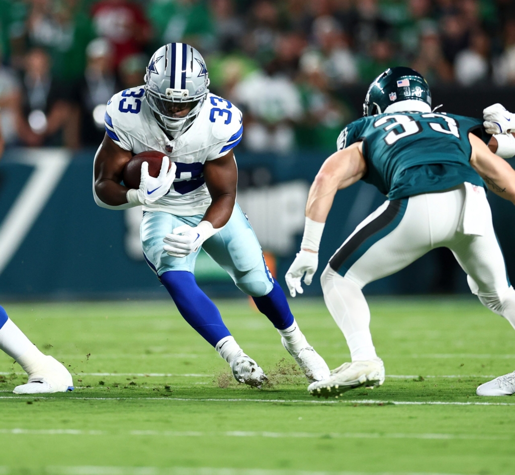 Running back in Dallas Cowboys jersey carrying the football past an opponent during an NFL game.