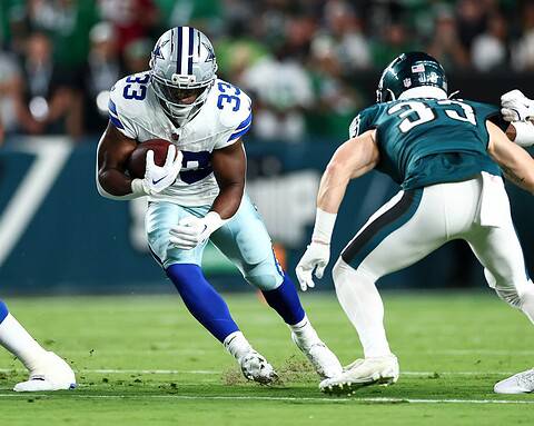 Running back in Dallas Cowboys jersey carrying the football past an opponent during an NFL game.