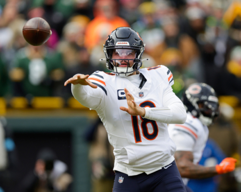 Quarterback Justin Fields in action during an NFL game, wearing Chicago Bears uniform, passing football on the field with a blurred crowd background.