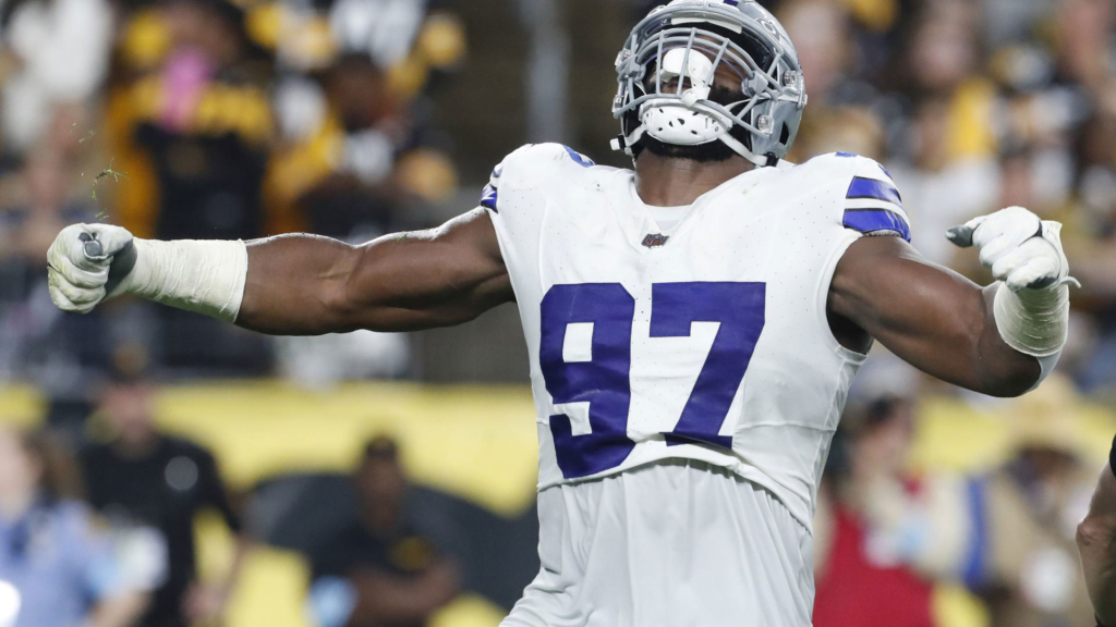 Athletic football player wearing jersey number 97 celebrating on the field during a game, showcasing strength and victory. Dallas Cowboys linebacker in action with a crowd in the background.