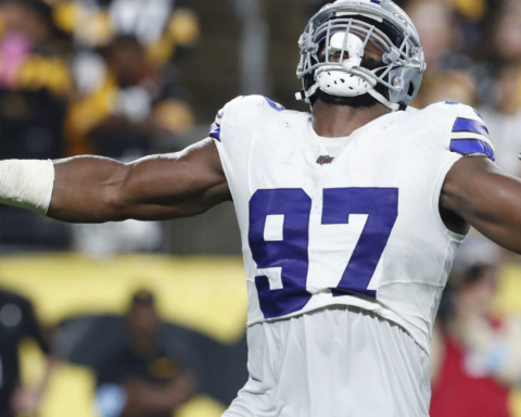 Athletic football player wearing jersey number 97 celebrating on the field during a game, showcasing strength and victory. Dallas Cowboys linebacker in action with a crowd in the background.