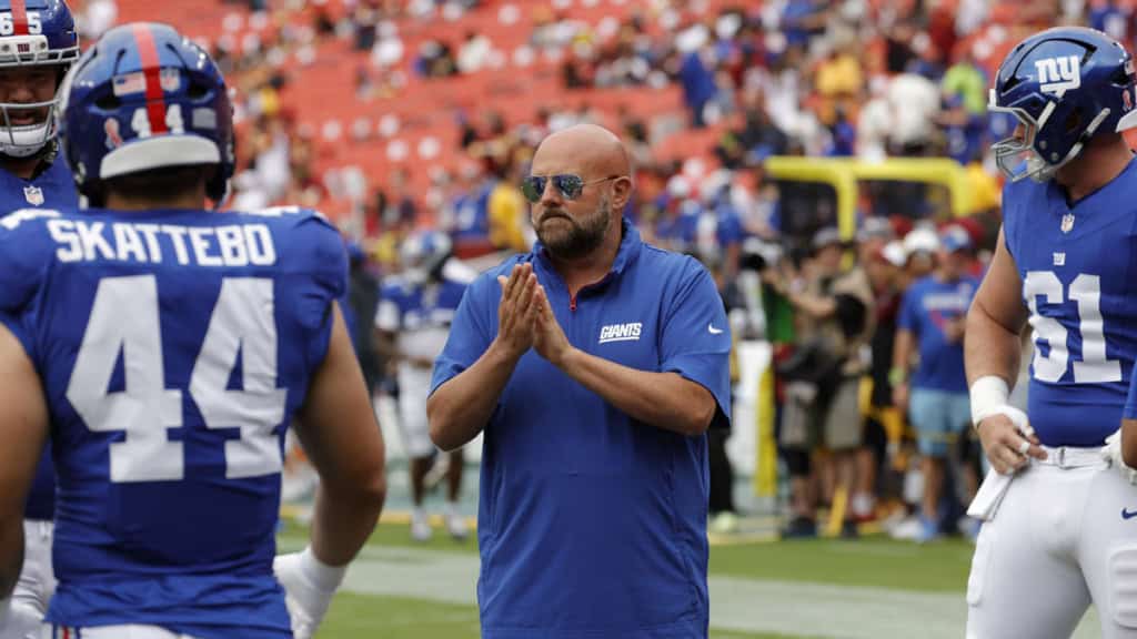 Thrilled New York Giants coach on sideline during football game, wearing team gear, coaching players amid stadium crowd, showcasing football strategy, teamwork, and NFL passion.