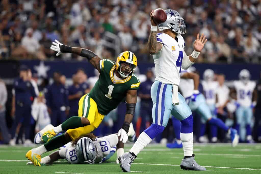 Passer in action for the Dallas Cowboys during an NFL game against the Green Bay Packers, with a Packers defender attempting a tackle; American football game at a packed stadium.