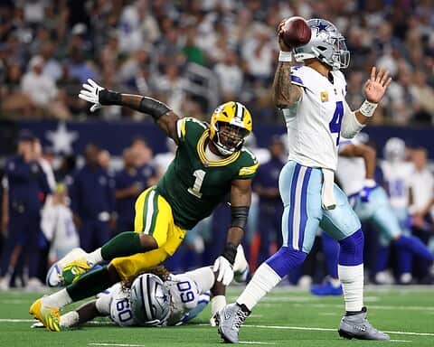 Passer in action for the Dallas Cowboys during an NFL game against the Green Bay Packers, with a Packers defender attempting a tackle; American football game at a packed stadium.