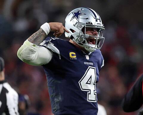 Cowboys quarterback Dak Prescott celebrating on the field during an NFL game. He is wearing a navy blue Dallas Cowboys jersey and #4 helmet with a silver star logo.