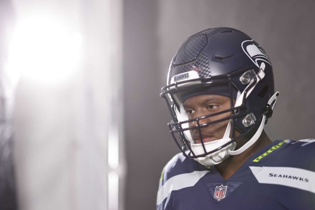 Seahawks football player wearing helmet and uniform, preparing for game at Lumen Field.
