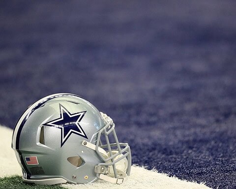 Dallas Cowboys football helmet on the field, close-up, showcasing team logo and American flag detail, with a background of the football field turf. Perfect for NFL and Dallas Cowboys fan content.