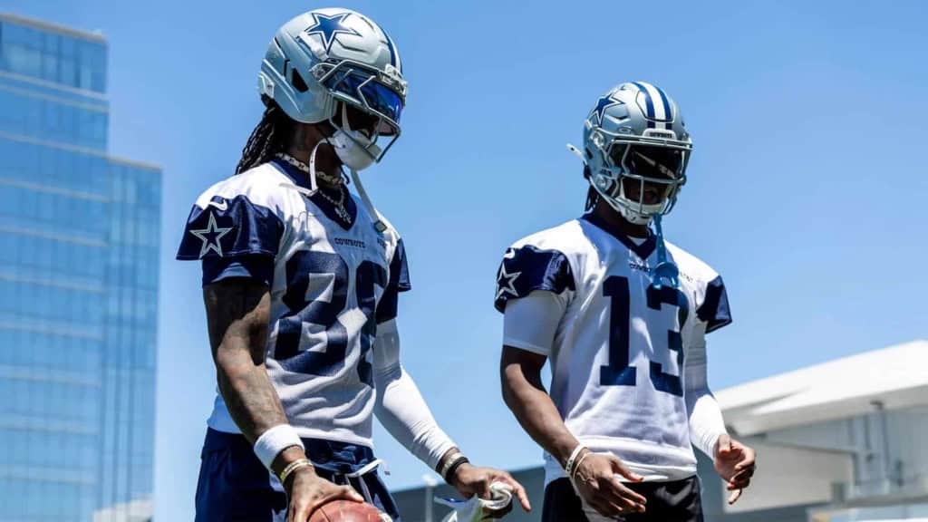 Dallas Cowboys football players wearing helmets and uniforms during a practice session on a sunny day.