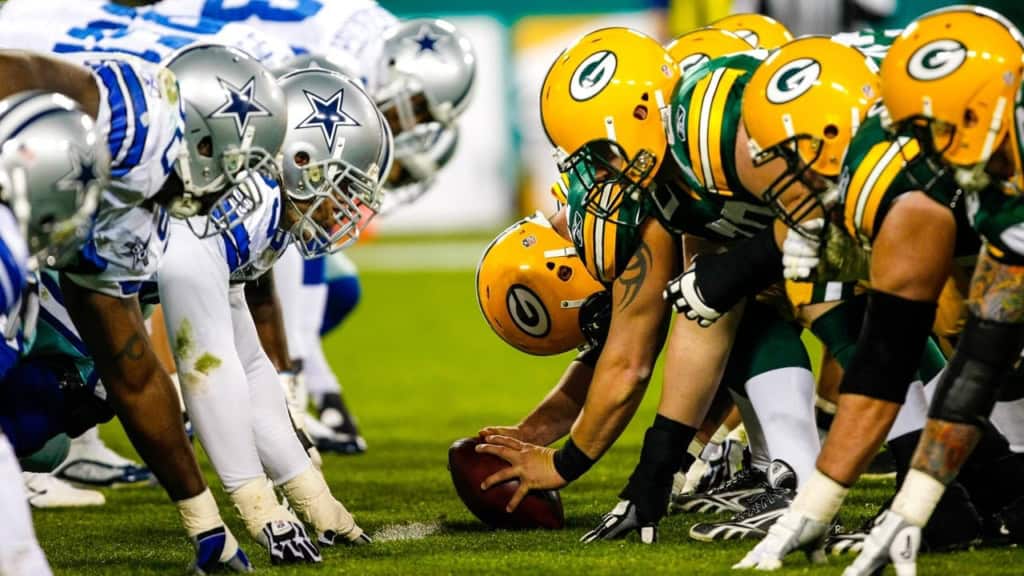 Dallas Cowboys vs Green Bay Packers football game showing line of scrimmage with players in helmets and pads.