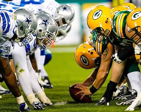 Dallas Cowboys vs Green Bay Packers football game showing line of scrimmage with players in helmets and pads.