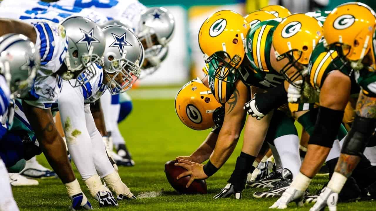 Dallas Cowboys vs Green Bay Packers football game showing line of scrimmage with players in helmets and pads.