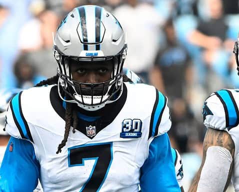 Bold move by the Carolina Panthers football player on the field during a game. The athlete is wearing a white and blue jersey with number 7, helmet, and pads, showing focus and determination. The background features other players and spectators, capturing the intensity of an NFL game. The image celebrates NFL football, Panthers team spirit, and player dedication. Perfect for sports fans and fans of the Carolina Panthers.