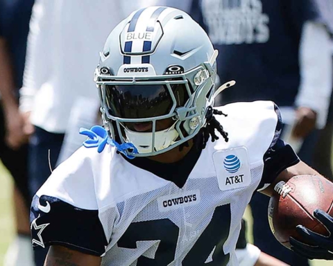 Dallas Cowboys football player in action during practice, wearing helmet and jersey, holding football, focusing on game strategy and team preparation.