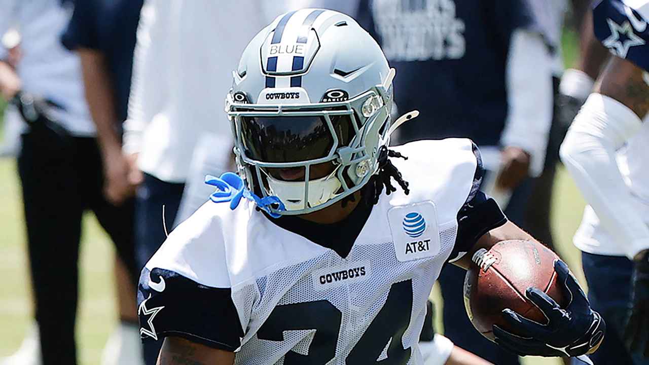 Dallas Cowboys football player in action during practice, wearing helmet and jersey, holding football, focusing on game strategy and team preparation.