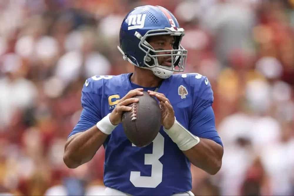 Quarterback Daniel Jones in official New York Giants uniform during game, holding football on the field.