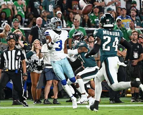 Dallas Cowboys wide receiver catching football during game against Philadelphia Eagles, with fans and cheerleaders in the background.